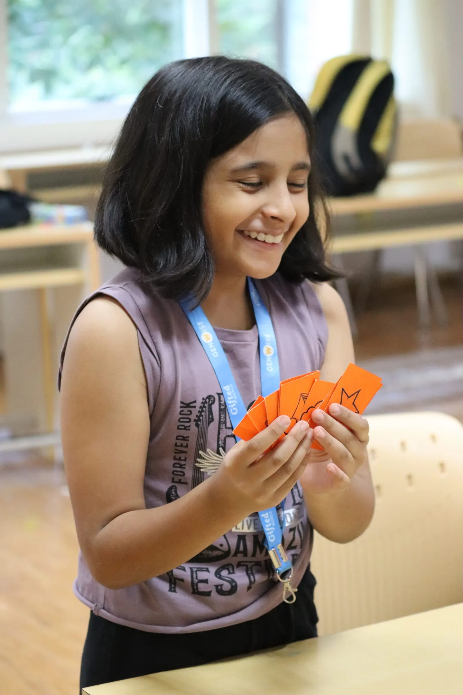 A GenWise student laughing while holding a fan of hand-drawn activity cards