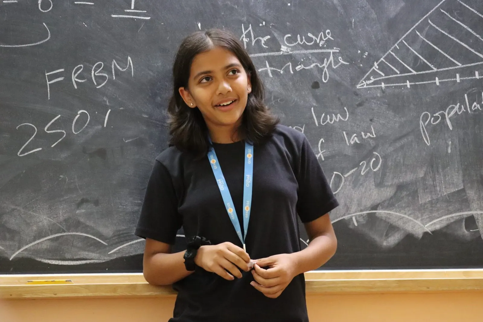 A GenWise student smiling at a chalkboard covered in economics notation